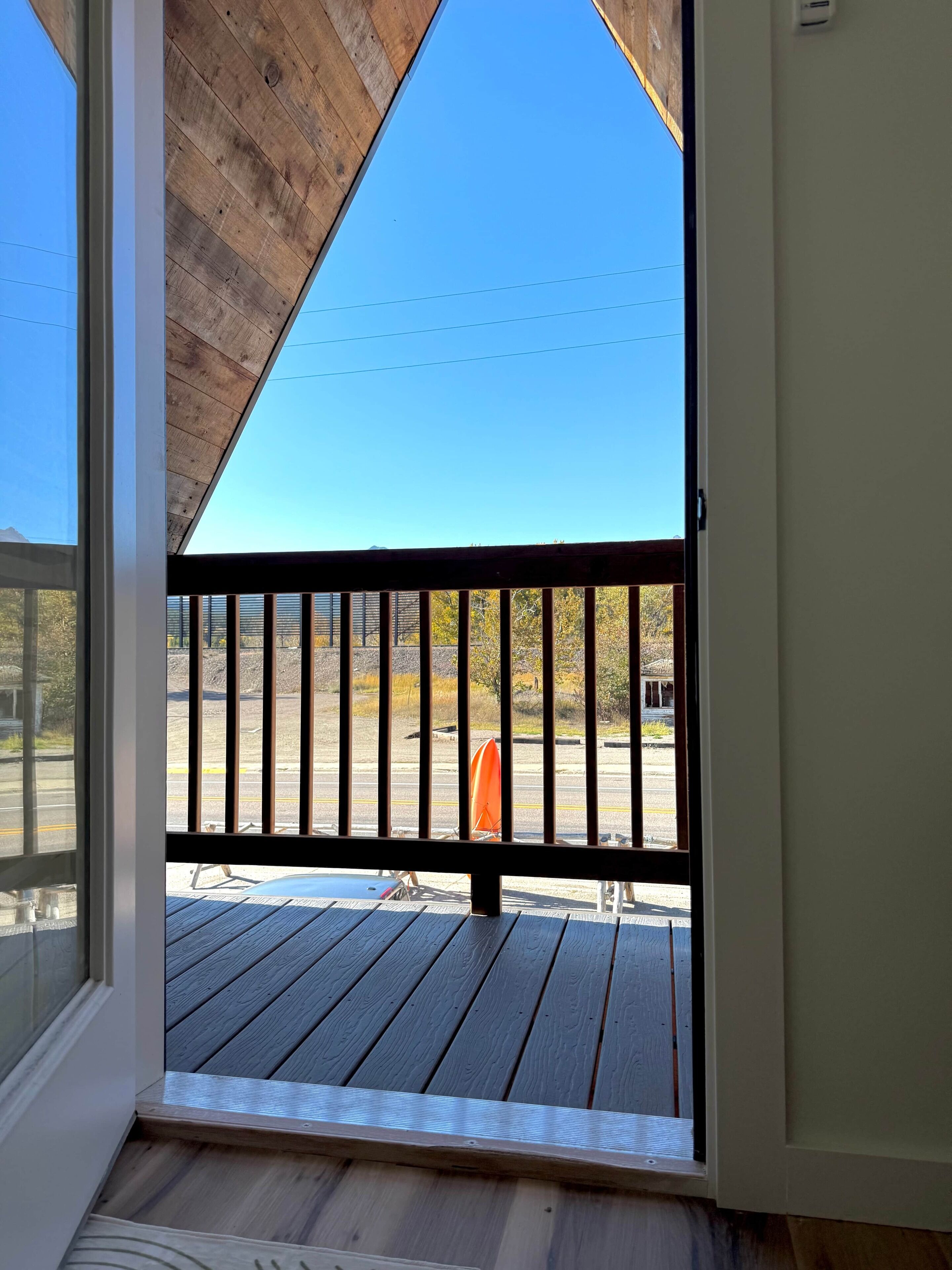 A wooden deck with a metal railing, a clear sky, and a view of a parking lot with a red object.