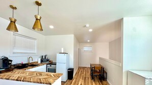 Une cuisine moderne avec un plan de travail en bois, un évier, une cuisinière et un réfrigérateur. On y trouve deux lampes suspendues et une fenêtre avec des stores.