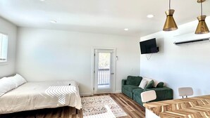 Une chambre moderne avec un plancher en bois, un lit, un canapé vert, une petite table et un téléviseur fixé au mur.