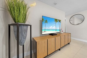 A modern living room with a flat-screen TV on a wooden console, a large potted plant, and a round mirror on the wall. - Casa Verde - 5 BDRM / 2 BA with POOL + HOT TUB (Miami)