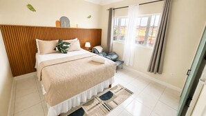 A bedroom with a bed, bedside table, lamp, chair, and a view through a window. - NEW! Hilltop Escape with Ocean Views (Montego Bay)