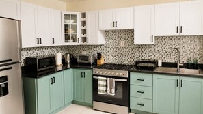 A kitchen with white cabinets, a stove, a microwave, and a refrigerator.