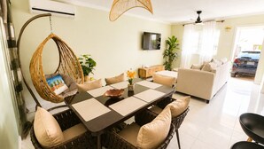 A dining area with a round table, wicker chairs, a hanging chair, and a TV on the wall. - NEW! Hilltop Escape with Ocean Views (Montego Bay)