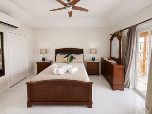 Una camera da letto con un letto di legno, due comodini, una ventola a soffitto, uno specchio grande e una finestra con tende.