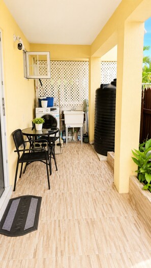 Un pequeño patio con una mesa, sillas, lavadora, tanque de agua y una puerta con felpudo.