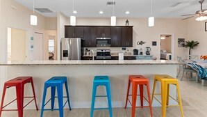 Une cuisine moderne avec des meubles de couleur sombre, un îlot central doté de tabourets et un éclairage suspendu au plafond.