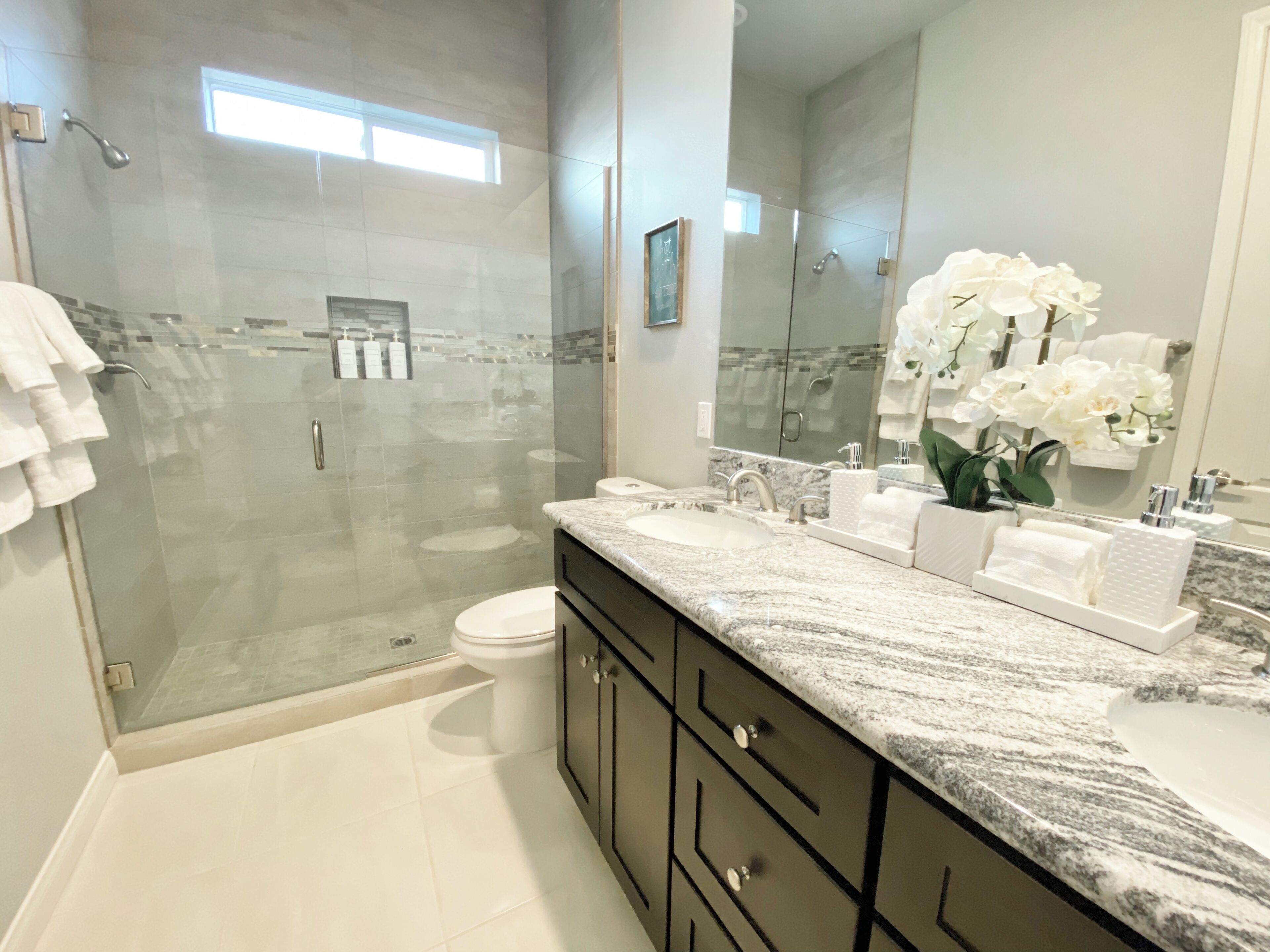 A modern bathroom with a glass-enclosed shower, a marble sink, and a large mirror.
