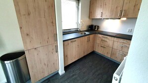 A compact kitchen with wooden cabinets, a stainless steel sink, and a window with blinds. - Bright & Modern Bungalow in Ejwik (Ewijk)