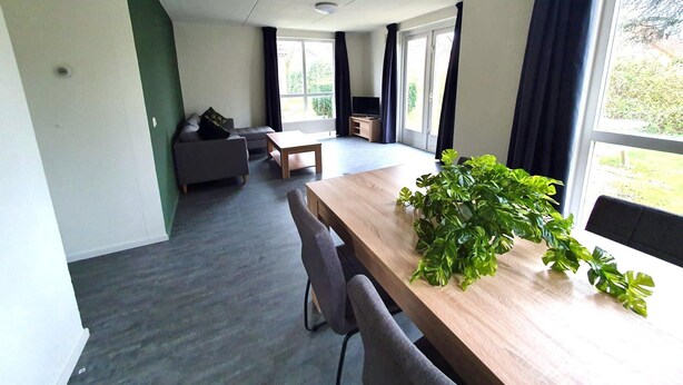 A modern living room with a sofa, a coffee table, and a dining area with a plant. - Bright & Modern Bungalow in Ejwik (Ewijk)