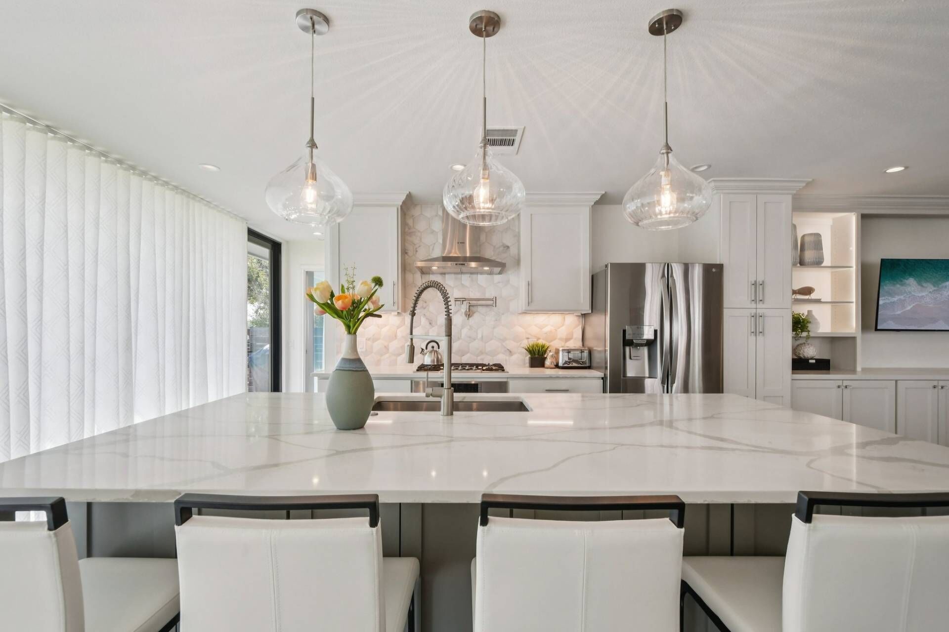A modern kitchen with a large island, pendant lights, and stainless steel appliances.