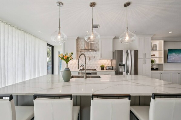 A modern kitchen with a large island, pendant lights, and stainless steel appliances.
