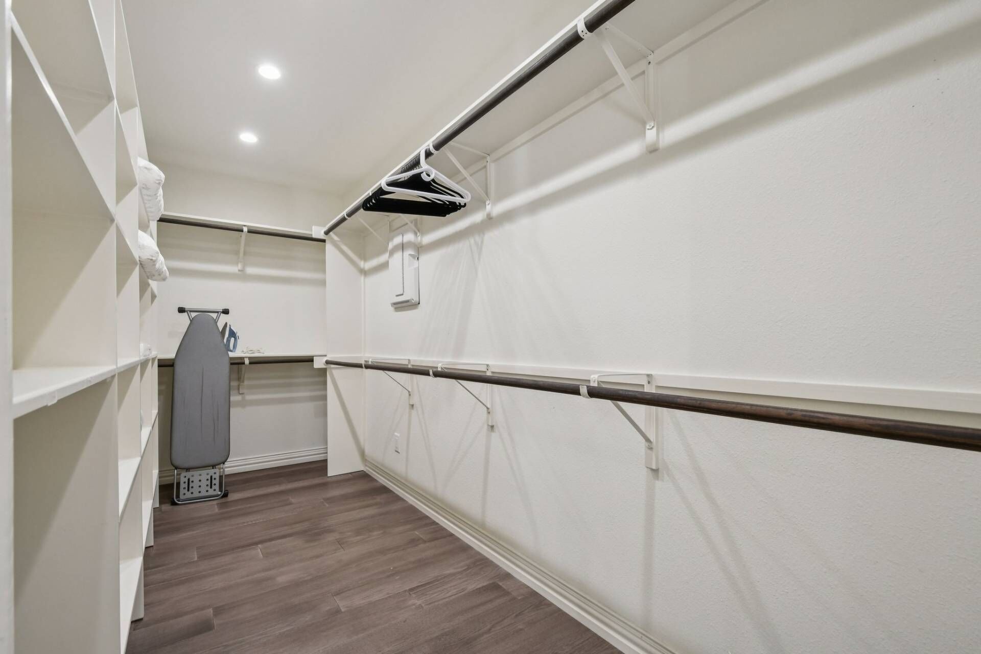 Un vestidor con piso de madera, paredes blancas y una barra metálica para colgar ropa.