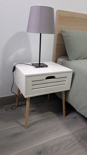 Une table de chevet avec une lampe, un tiroir et un câble d’alimentation.