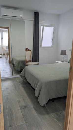 Quarto com cama, cadeira, escrivaninha, janela e ar condicionado.