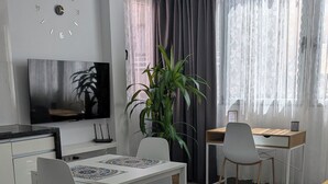 A modern living room with a dining table, chairs, a TV, a plant, and a window with curtains. - Apartment near the airport, The Greey's house D (El Calero)