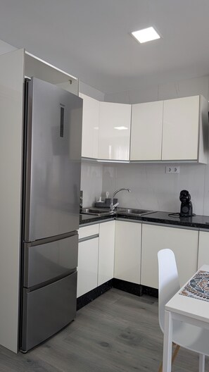 A compact kitchen with white cabinets, a stainless steel refrigerator, a black countertop, and a coffee maker.