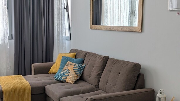 A modern living room with a brown sofa, a small white table, and a mirror on the wall. - Apartment near the airport, The Greey's house D (El Calero)