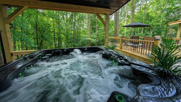 Un jacuzzi con terraza de madera y vistas a un bosque.