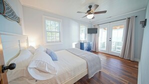Un dormitorio con cama, ventilador de techo, televisor y vistas al exterior a través de una puerta corredera.
