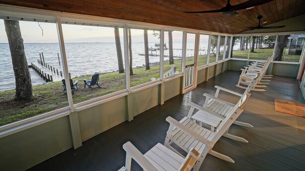 Una terraza techada con sillas Adirondack blancas, techo de madera y vista al agua.
