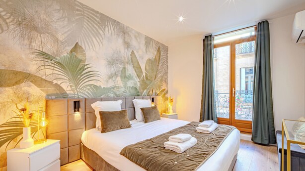 Un dormitorio con una cama grande, una mesita de noche, una lámpara, un mural en la pared y vistas al balcón exterior.