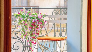 Un balcón con barandilla metálica, un cojín y flores colgantes.