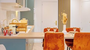 Una cocina moderna con encimera de madera, dos lámparas colgantes y un comedor con sillas tapizadas en naranja y una mesa blanca.