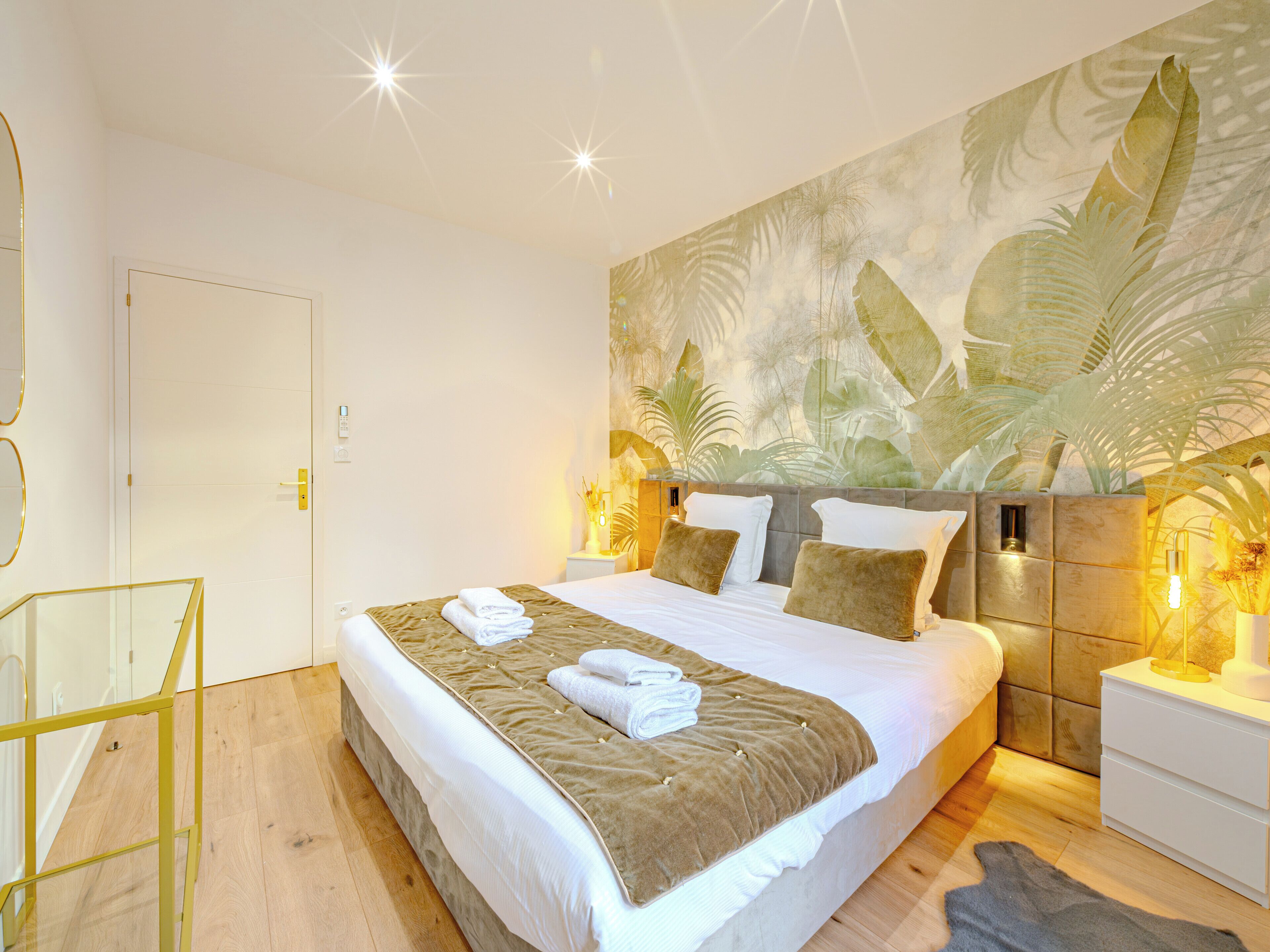 A modern hotel room with a large bed, a glass desk, and a tropical-themed wall mural.