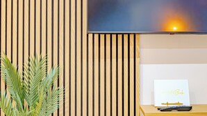 Una habitación con pared de listones de madera, un televisor de pantalla plana montado sobre un escritorio de madera, y un cartel en el escritorio que dice 'Guest Book'.