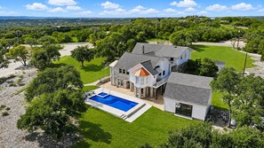 A large house with a swimming pool, surrounded by lush greenery and a clear sky.