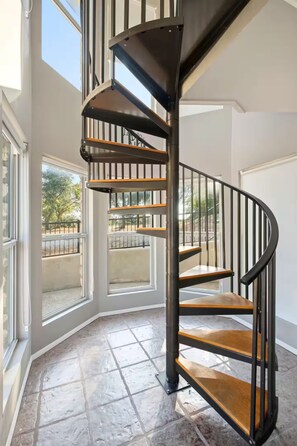 Un escalier en colimaçon avec des marches en bois et des rampes noires, menant à l’étage supérieur.