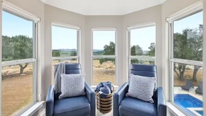 A room with two leather chairs, a small woven basket, and large windows offering a view of a pool and landscape. - NEW! Lake View • Pool + Spa • Game Room • Fire Pit • Near Marina & Wineries (Canyon Lake)