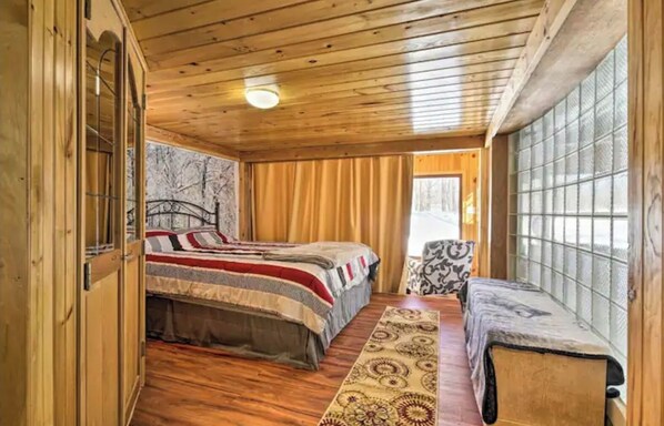 A wooden cabin bedroom with a bed, a chair, a window, and a door. - Relaxing Inn Kinzua (Russell)