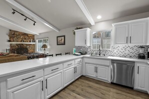 A modern kitchen with white cabinetry, a stone accent wall, and a built-in dishwasher. - The Wolf House-Best Mountain View’s. (Big Bear Lake)