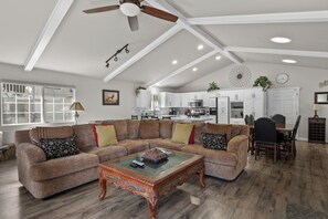 Un salon spacieux avec un canapé d’angle, une table basse en bois et un ventilateur de plafond.