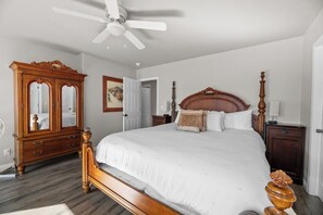 Une chambre à coucher avec un grand lit, une commode en bois, un ventilateur de plafond et un tableau accroché au mur.