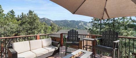 A deck with a sofa, chairs, a fire pit, and a large umbrella.
