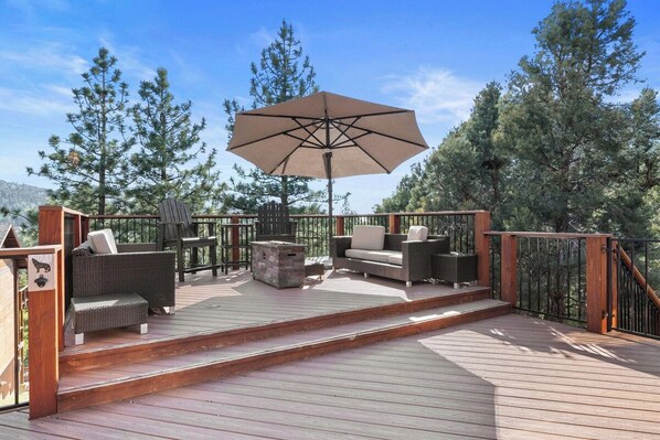 A wooden deck with outdoor furniture, including a sofa, chairs, and a table, under a large umbrella.