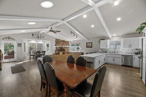 Une cuisine spacieuse avec des meubles blancs, une table à manger en bois et un ventilateur de plafond.