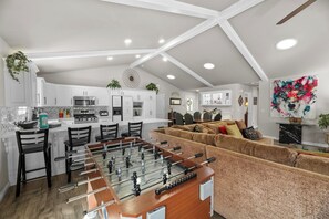 Un grand espace de vie comprenant une table de baby-foot, un canapé et une table à manger avec des chaises.