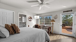 A bedroom with a bed, a desk, a chair, a ceiling fan, a window, and a door leading to an outdoor deck. - The Wolf House-Best Mountain View’s. (Big Bear Lake)