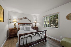 A bedroom with a wooden bed, two bedside tables with lamps, a window with a view, and a decorative wall piece. - The Wolf House-Best Mountain View’s. (Big Bear Lake)