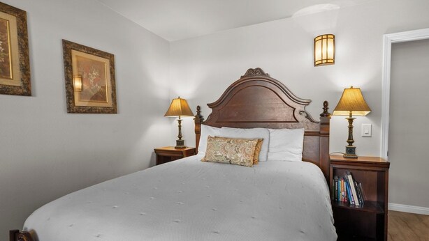 A neatly made bed with a headboard, two bedside lamps, and a nightstand with books. - The Wolf House-Best Mountain View’s. (Big Bear Lake)