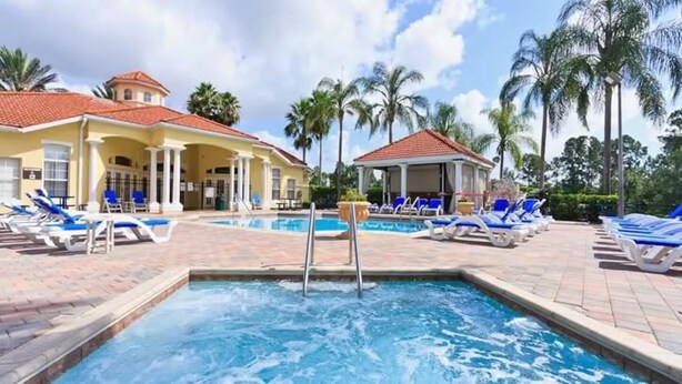 A pool area with lounge chairs and a building with a red-tiled roof.