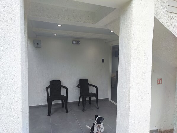 Un espacio de estar al aire libre techado con dos sillas y un perro.