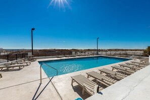 Un ciel d’un bleu éclatant, une piscine bordée de chaises longues et, au loin, une plage de sable.
