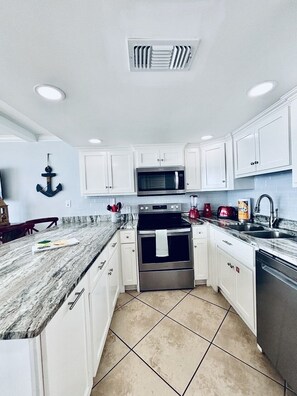 A modern kitchen with white cabinets, a stainless steel oven, a microwave, and a granite countertop.
