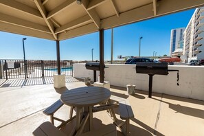 An outdoor patio with a pool, barbecue grills, and a table with benches.
