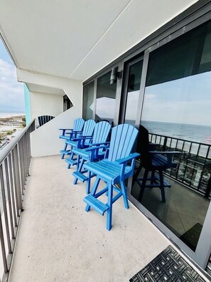 A balcony with blue chairs and a glass door leading to a view of the ocean.