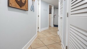 A hallway with a wooden anchor decoration, a sign reading "BEACH HOUSE," and a door with a louvered design. - Islands Winds East - Unit 506 (Gulf Shores)